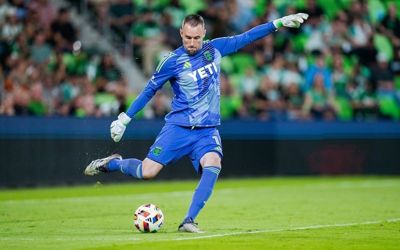 Torwart in blauem Trikot schlägt den Fußball mit dem Fuß weg
