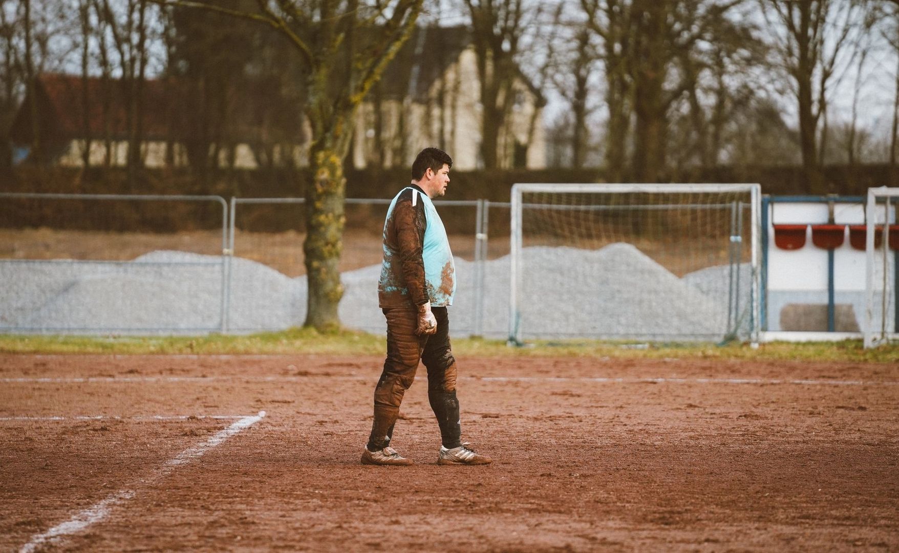 Fußballspieler steht auf einem matschigen Amateurplatz vor dem Tor